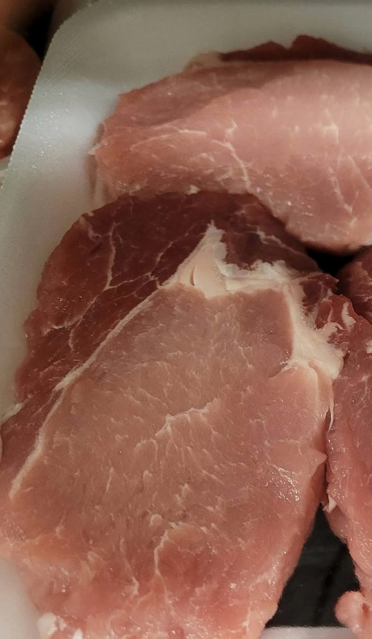 Pork loin chops laid out on a white tray, cut thick.