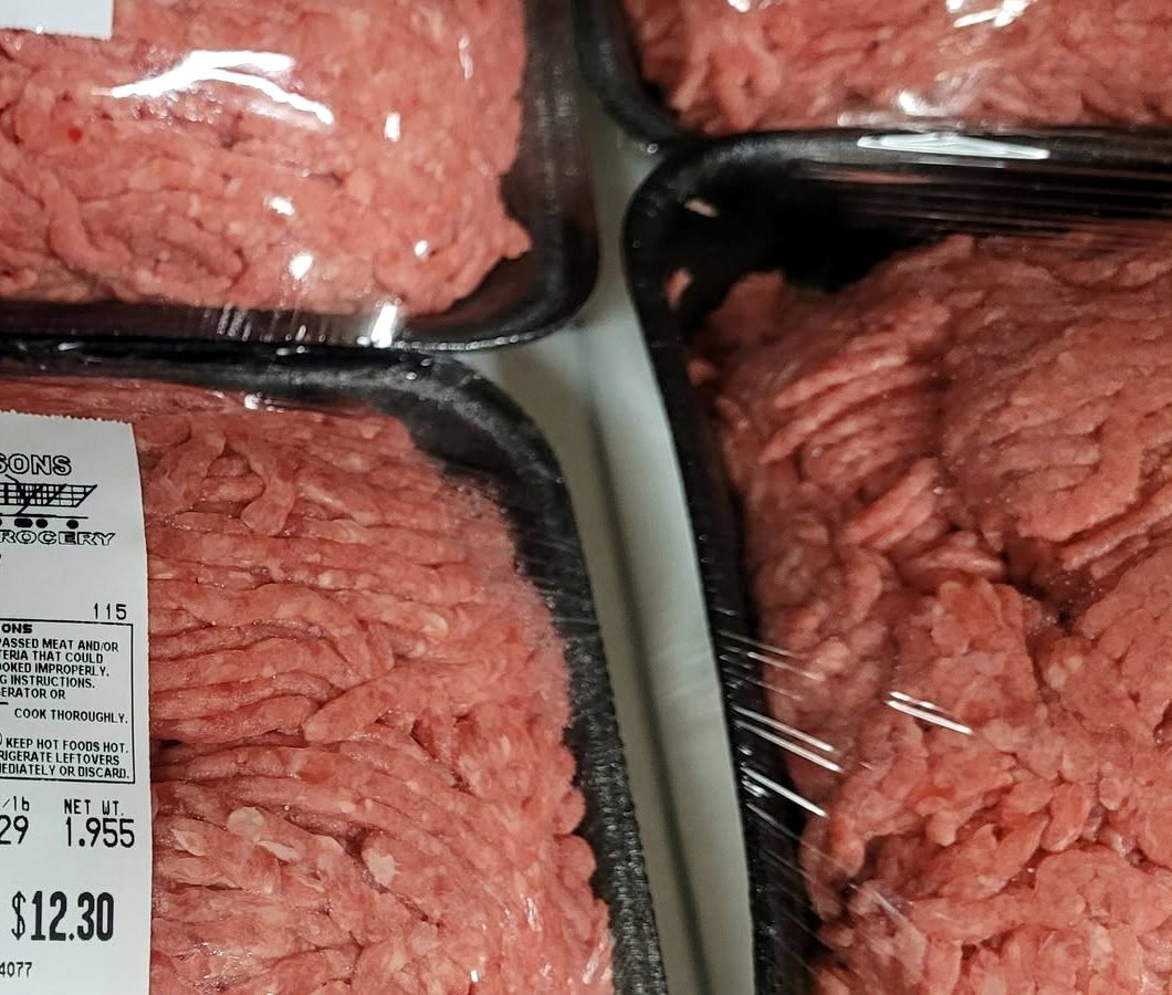 Trays of freshly ground beef, wrapped in film, side by side in a chilled case.