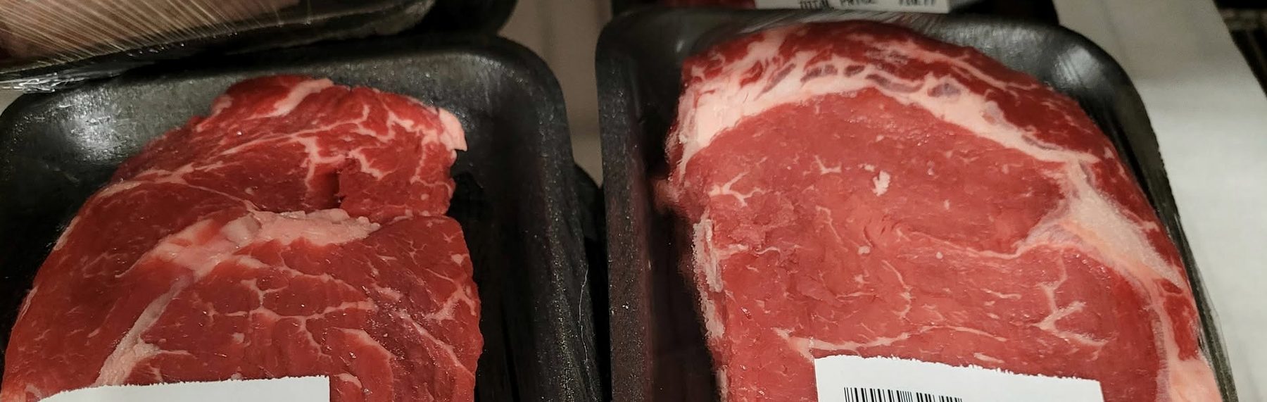 Two ribeye steaks side by side on black foam trays in the service case.